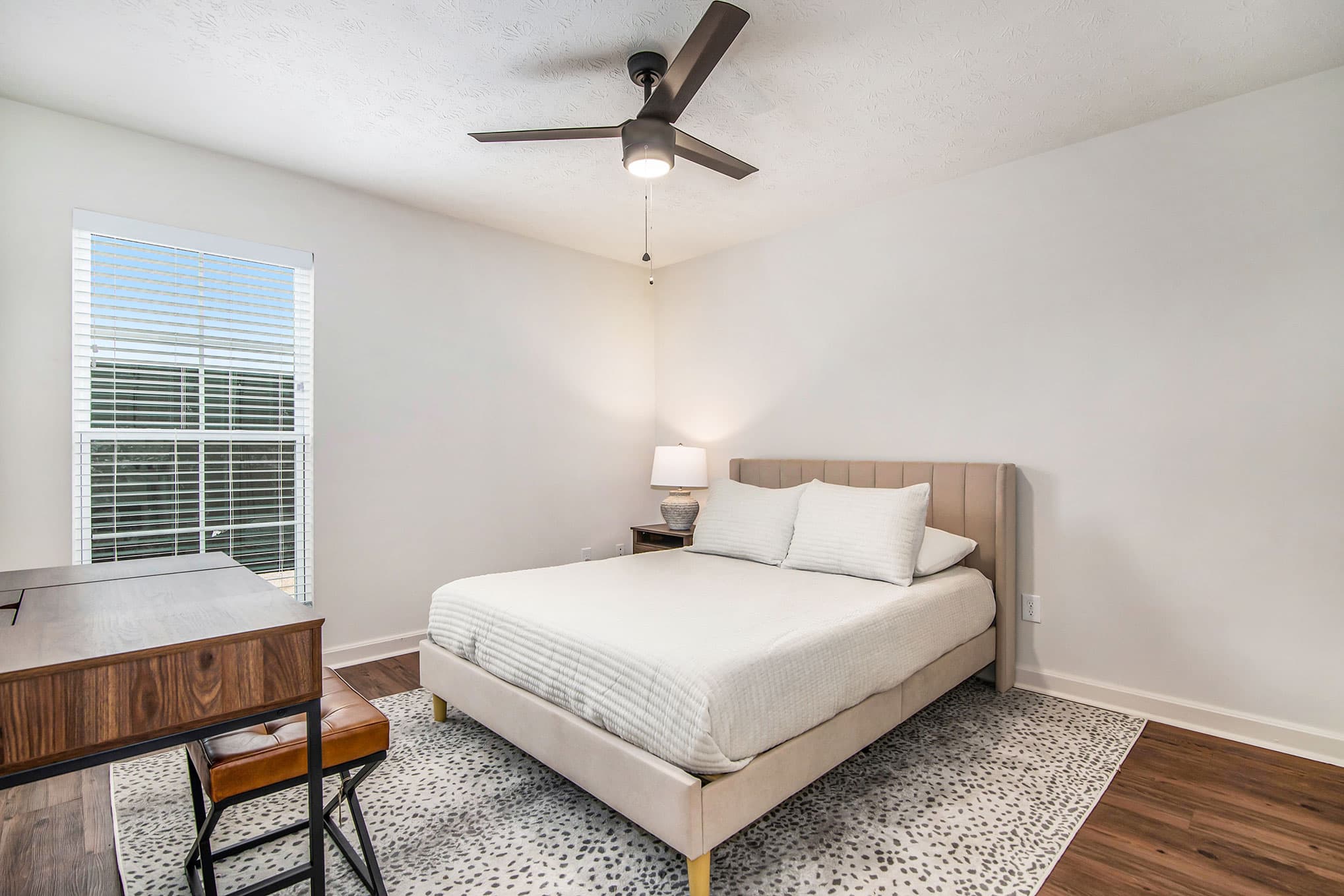 Second bedroom with upholstered headboard, desk, and ceiling fan